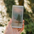 Gallery viewerに画像を読み込む, A hand holds a Viwoods AiPaper Reader Colour product outdoors against a blurred green bokeh background. The device screen is illuminated with a soft landscape illustration and the text 'Think Better, on Paper'.