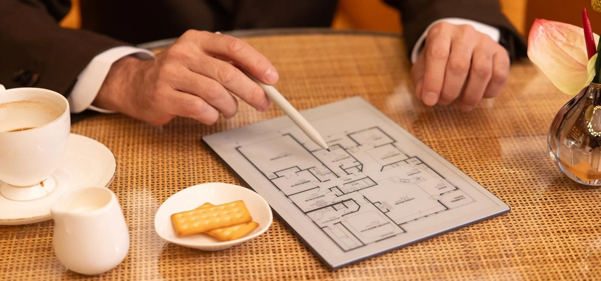 Person holding a pen over a map on a viwoods paper table with a cup of coffee and cookies.